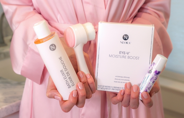 Woman holding Neora’s Make Her Mother’s Day Bundle which includes: Zen + Calm Lavender Balm, Bath Elixir, Eye-V Moisture Boost Hydrogel Patches and a FREE dual-sided Facial Scrubber